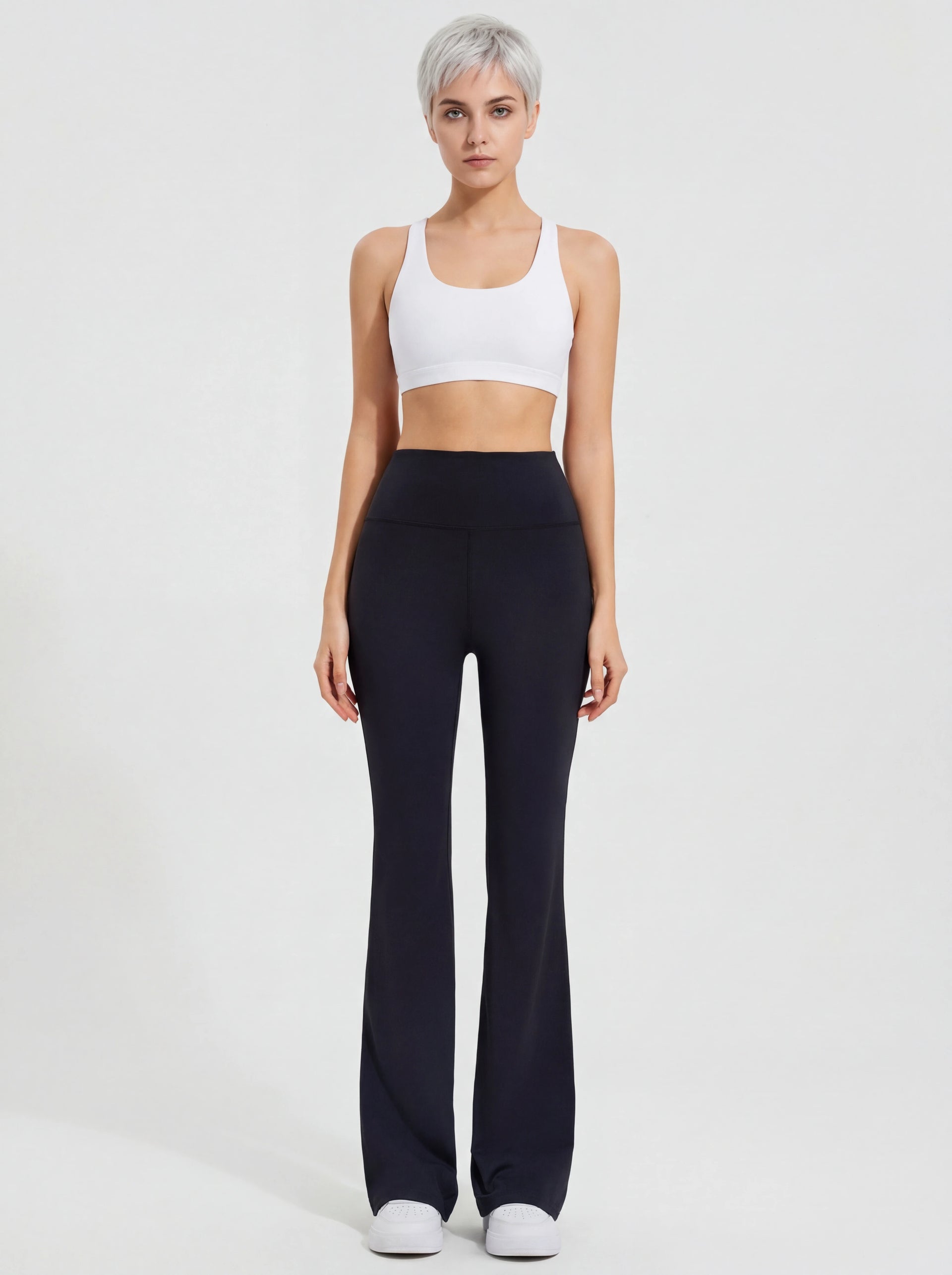 Woman wearing a white tank top and black high-waisted pants on a light gray background