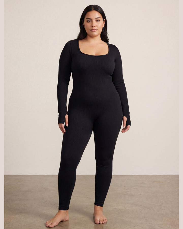 VLIZ Eclipse Ribbed Sculpting Jumpsuit; A female model showcases the full-length black activewear jumpsuit, featuring a form-fitting ribbed fabric, a square neckline, and long sleeves with thumbholes. It offers a supportive fit, suitable for gym workouts, yoga, Pilates, and everyday training.