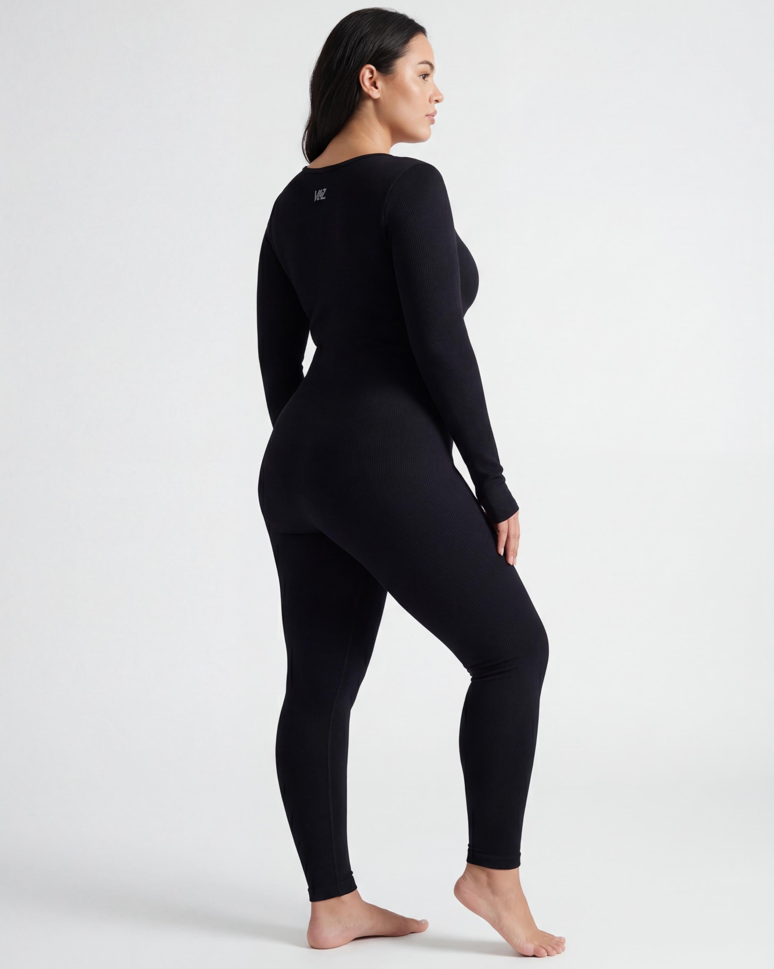 VLIZ Eclipse Ribbed Sculpting Jumpsuit; A female model showcases the full-length black activewear jumpsuit, featuring a form-fitting ribbed fabric, a square neckline, and long sleeves with thumbholes. It offers a supportive fit, suitable for gym workouts, yoga, Pilates, and everyday training.