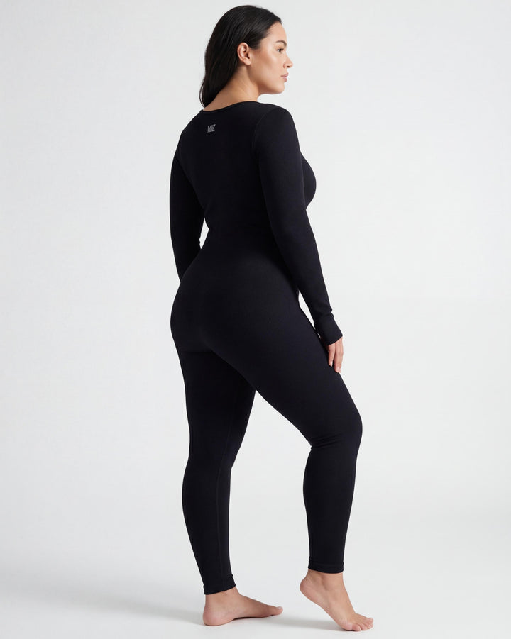 VLIZ Eclipse Ribbed Sculpting Jumpsuit; A female model showcases the full-length black activewear jumpsuit, featuring a form-fitting ribbed fabric, a square neckline, and long sleeves with thumbholes. It offers a supportive fit, suitable for gym workouts, yoga, Pilates, and everyday training.
