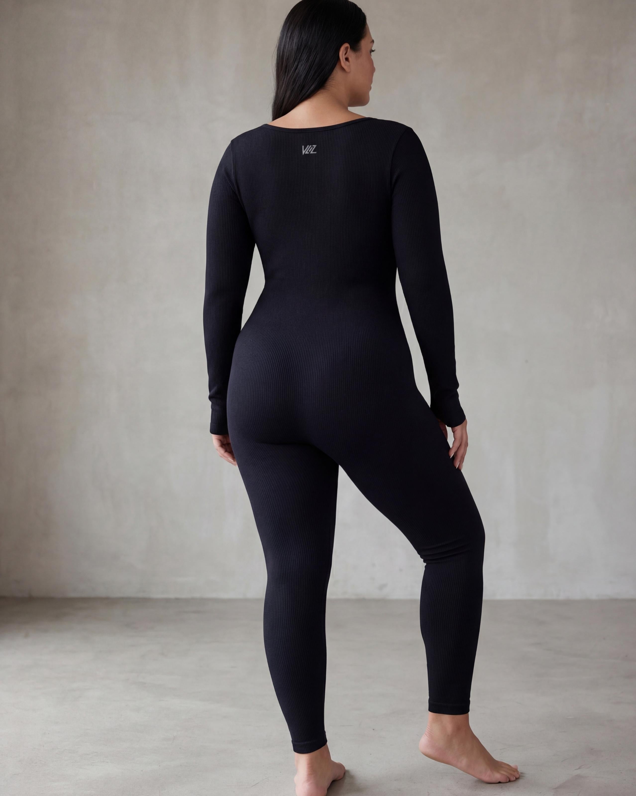 VLIZ Eclipse Ribbed Sculpting Jumpsuit; A female model showcases the full-length black activewear jumpsuit, featuring a form-fitting ribbed fabric, a square neckline, and long sleeves with thumbholes. It offers a supportive fit, suitable for gym workouts, yoga, Pilates, and everyday training.