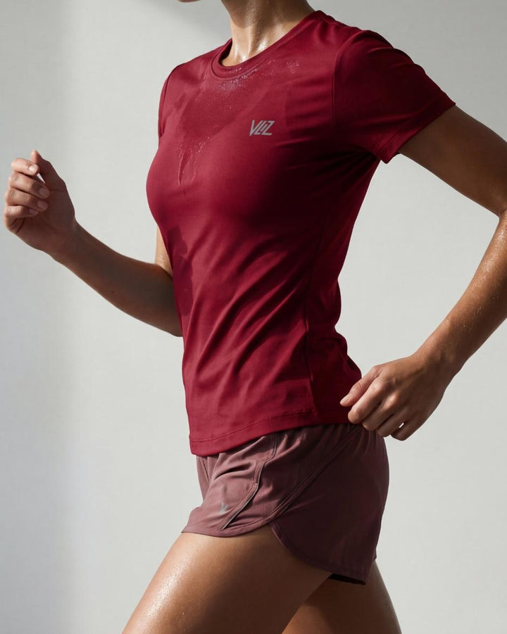 A model wears a form-fitting, short-sleeved deep red crew neck t-shirt. The smooth fabric highlights a comfortable, athletic fit suitable for workouts or casual wear.