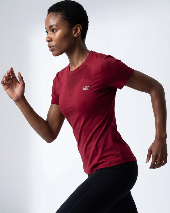 A model wears a form-fitting, short-sleeved deep red crew neck t-shirt. The smooth fabric highlights a comfortable, athletic fit suitable for workouts or casual wear.