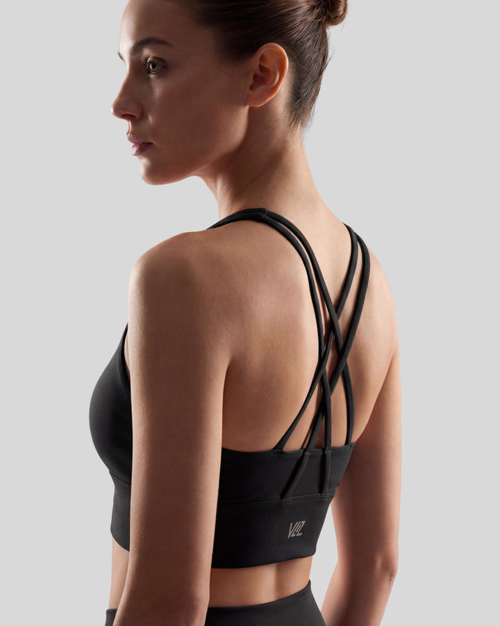 VLIZ Strappy-Back Sports Bra. A woman models the vibrant red/black sports bra with a high neckline and distinctive criss-cross back straps. The ribbed fabric provides a supportive fit, suitable for gym workouts, yoga, Pilates, and everyday training.