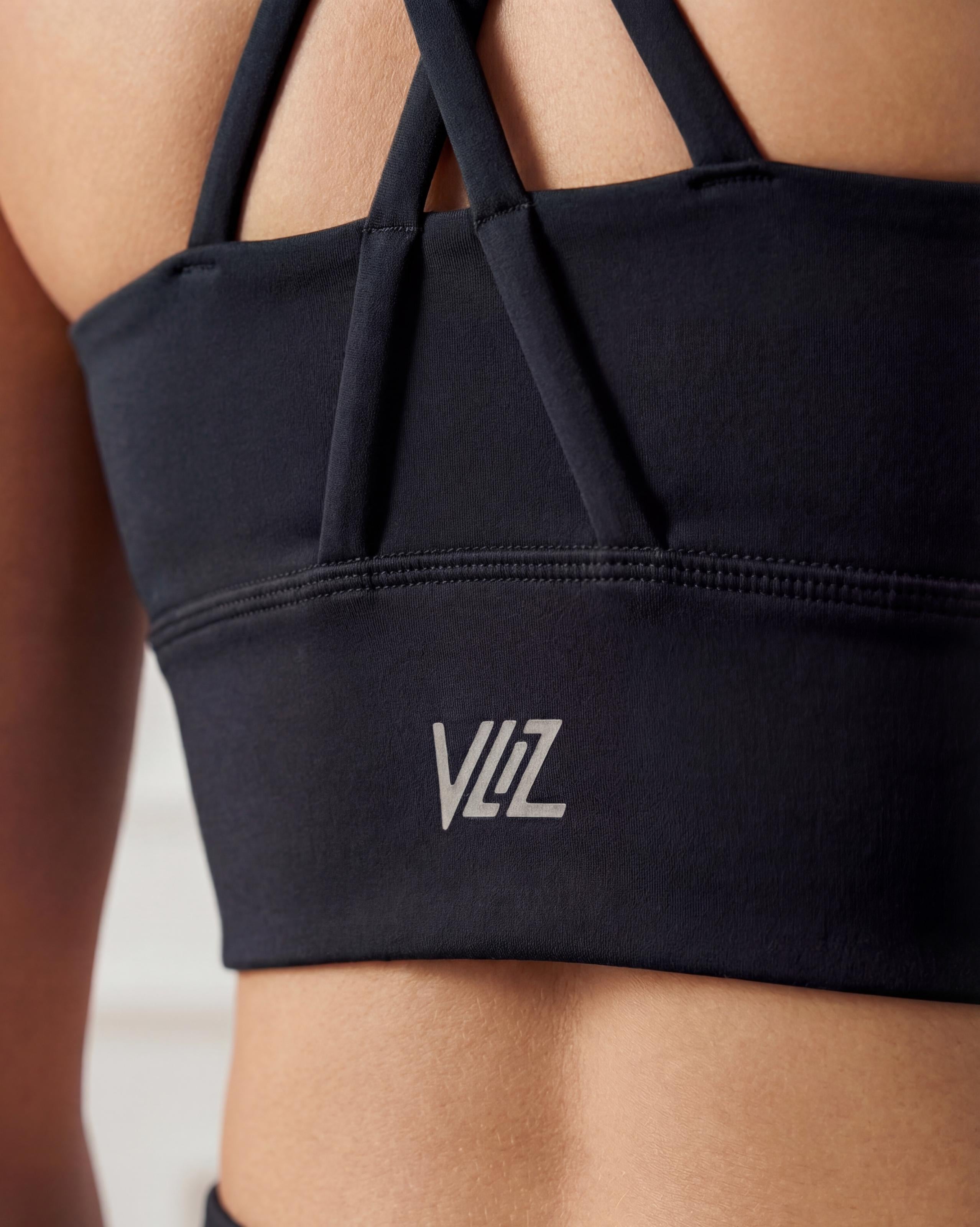 VLIZ Strappy-Back Sports Bra. A woman models the vibrant red/black sports bra with a high neckline and distinctive criss-cross back straps. The ribbed fabric provides a supportive fit, suitable for gym workouts, yoga, Pilates, and everyday training.