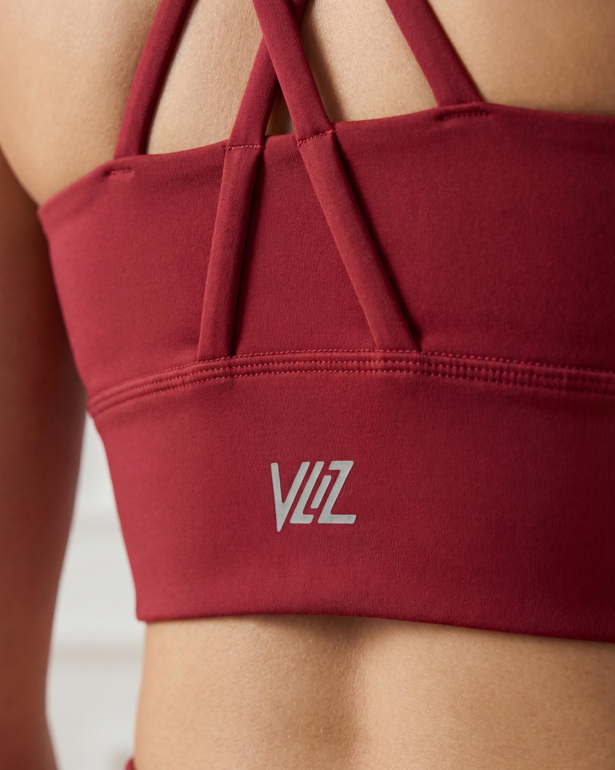 VLIZ Strappy-Back Sports Bra. A woman models the vibrant red/black sports bra with a high neckline and distinctive criss-cross back straps. The ribbed fabric provides a supportive fit, suitable for gym workouts, yoga, Pilates, and everyday training.
