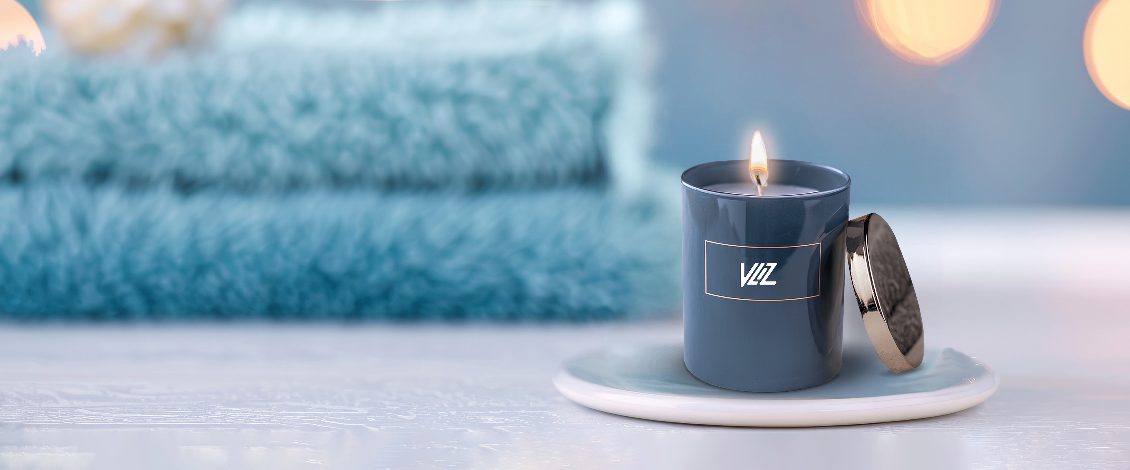 Luxurious dark blue VLIZ candle glowing softly on a ceramic tray, set against plush folded towels and warm bokeh lights — evoking calm, spa-like relaxation.