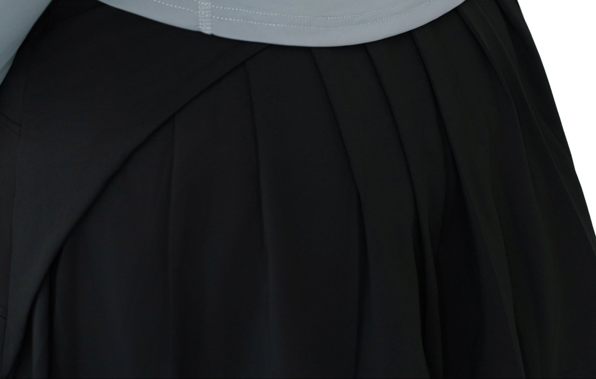 Close-up of the pleated back design on VLIZ ContourFlex Tennis Skirt in black, showing angled seam and waistline detail,