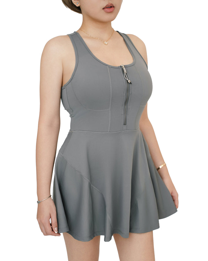 Side-angled front view of model wearing the gray VLIZ FlowFit Half Zip-Front Tennis Dress, highlighting the zip-front bodice and flared hem.