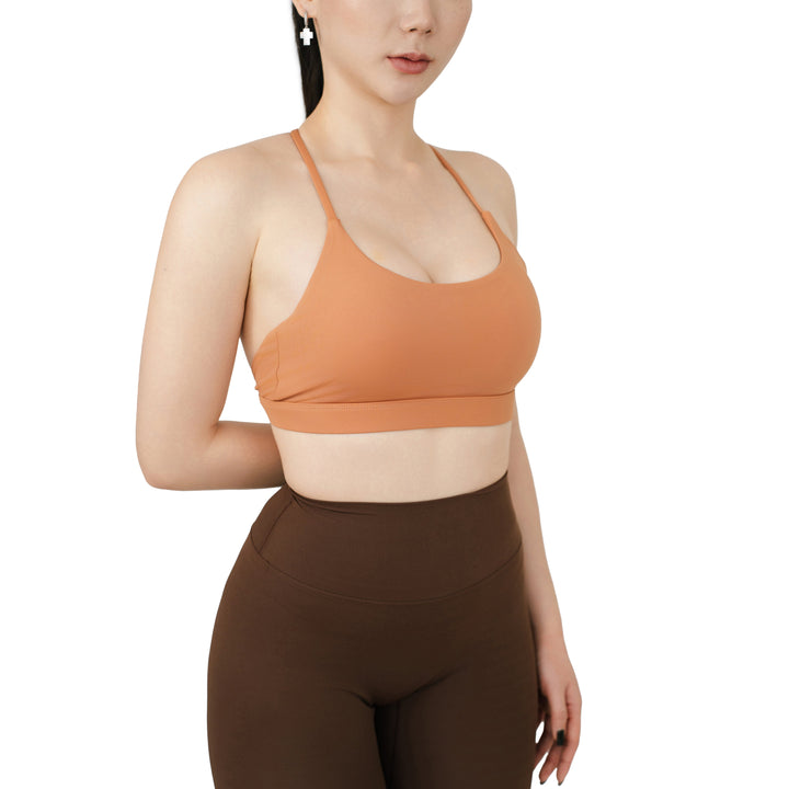 Angled front view of the VLIZ SculptFlex Cross-Back Sports Bra in Caramel Orange, showing the scoop neckline, sleek straps, and supportive fit.