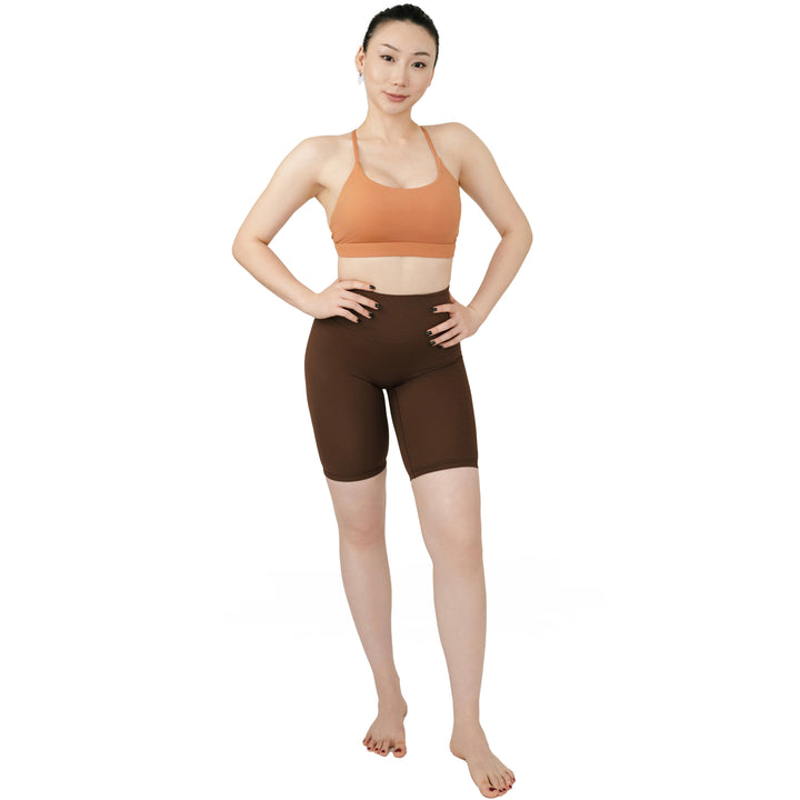 Full front view of the VLIZ SculptFlex Cross-Back Sports Bra in Caramel Orange, paired with high-rise brown biker shorts, showcasing its sleek fit and scoop neckline.