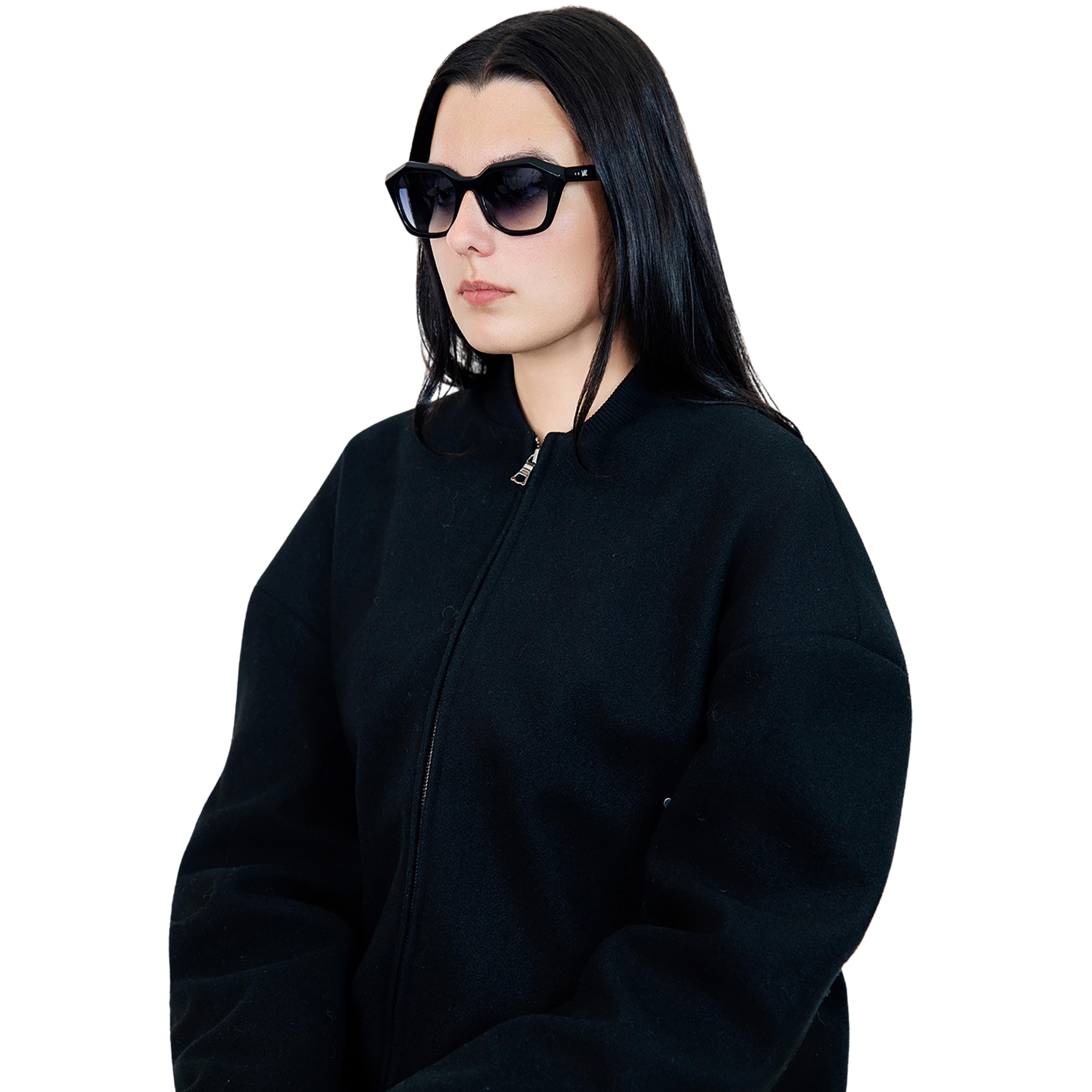 Model wearing VLIZ Altara sunglasses with a black square-oval frame and grey lenses, styled with a hoodie and layered necklace, emphasizing the unisex streetwear-inspired design and UV400 lens protection.