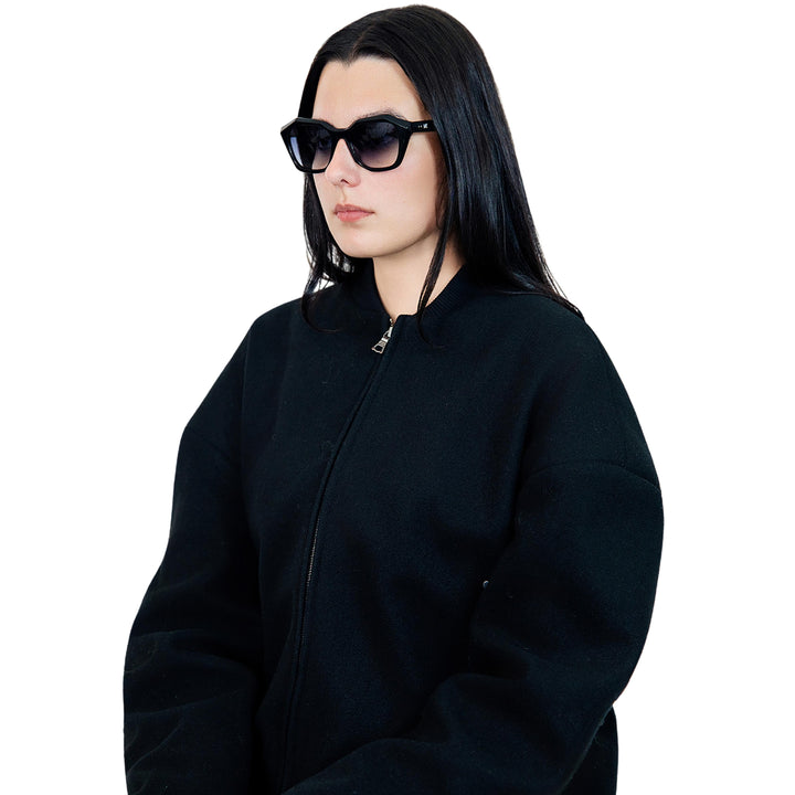 Model wearing VLIZ Altara sunglasses with a black square-oval frame and grey lenses, styled with a hoodie and layered necklace, emphasizing the unisex streetwear-inspired design and UV400 lens protection.