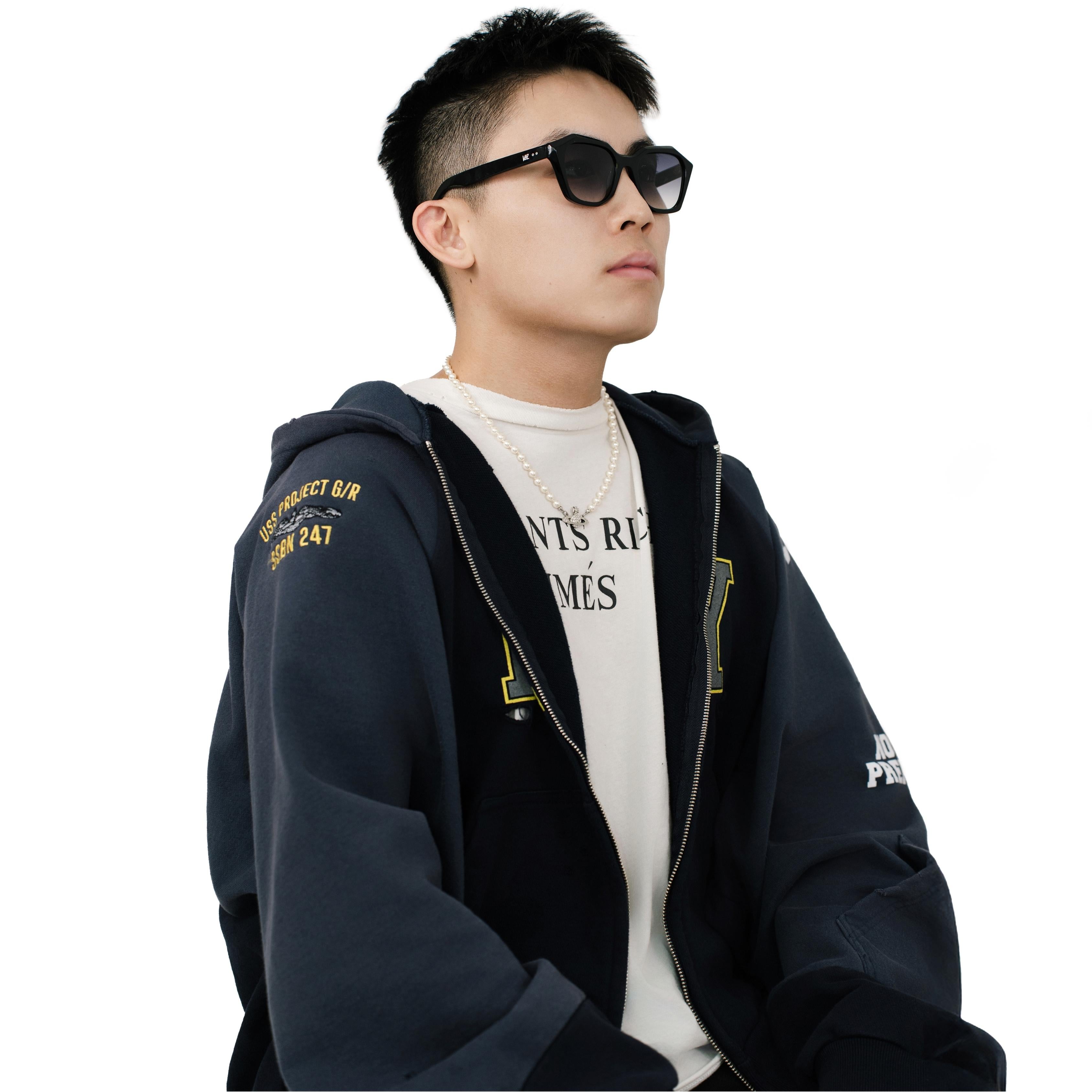 Model wearing VLIZ Altara sunglasses with a black square-oval frame and grey lenses, styled with a hoodie and layered necklace, emphasizing the unisex streetwear-inspired design and UV400 lens protection.