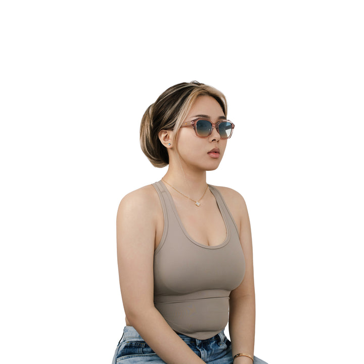 Model wearing VLIZ Altara sunglasses with a translucent pink-gradient frame and blue lenses, paired with a taupe sports tank and denim jeans, showing a soft yet modern unisex aesthetic with UV400 lens protection.