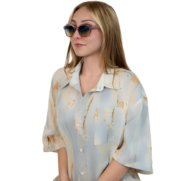 Model wearing VLIZ Altara sunglasses with a translucent pink-gradient frame and blue lenses, paired with a taupe sports tank and denim jeans, showing a soft yet modern unisex aesthetic with UV400 lens protection.