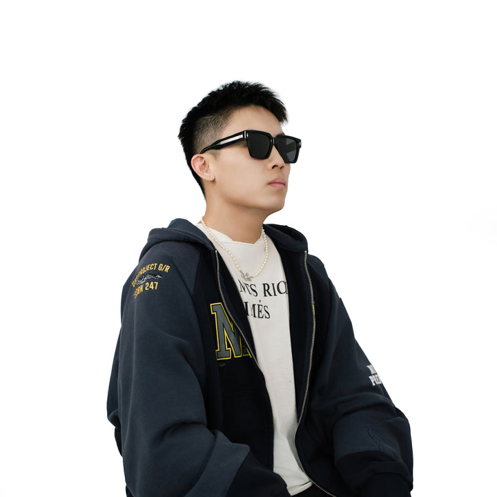Male model wearing VLIZ Gravité black square sunglasses with silver-tone temples and UV400 lenses, paired with a layered hoodie and graphic tee for an effortlessly cool streetwear look.