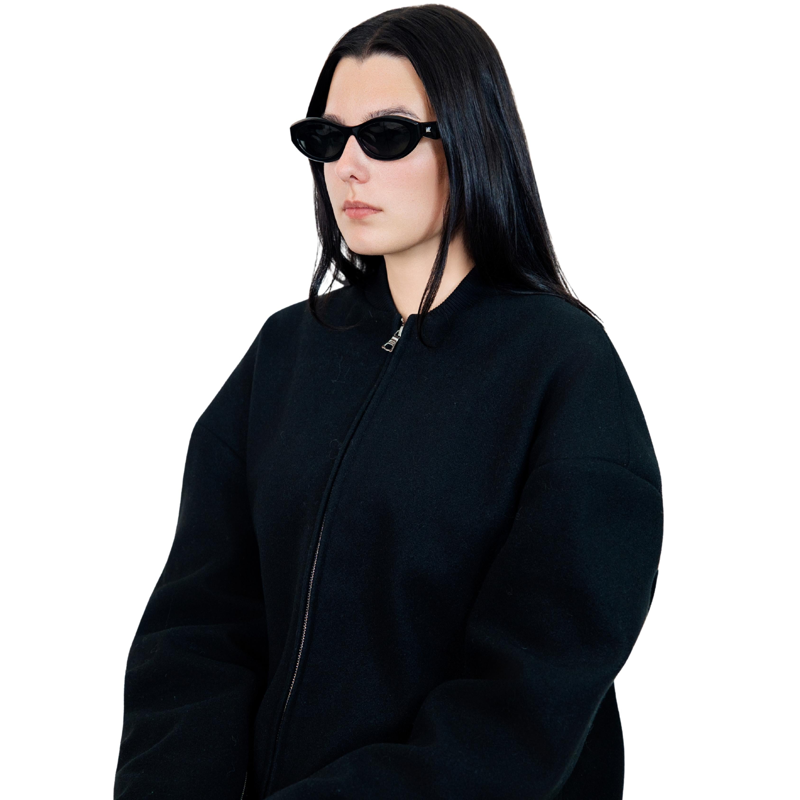 VLIZ Nolita oval sunglasses with black frame and black lenses, featuring smooth oval design and engraved logo on temples.