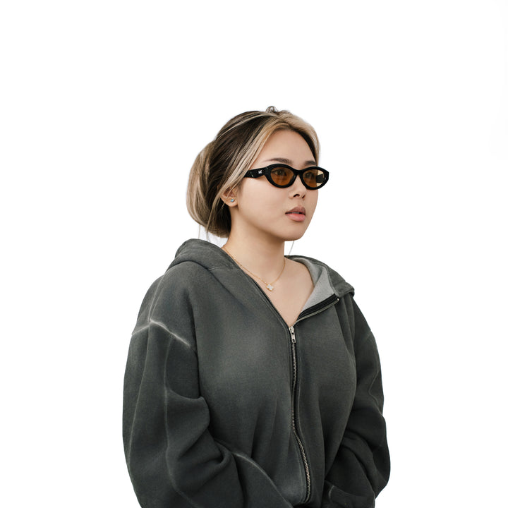 VLIZ Nolita oval sunglasses with black frame and brown lenses, featuring smooth oval design and engraved logo on temples.