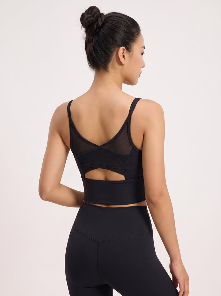 A woman shown from the back wearing a black sports bra with mesh back panels and a cutout, paired with black leggings, against a plain light background.