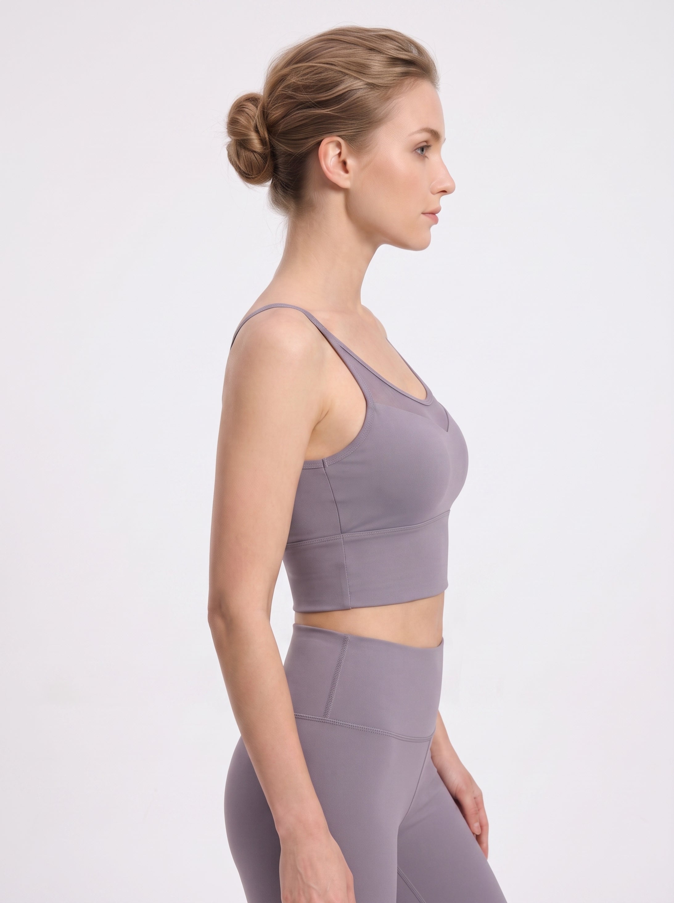A woman in side profile wearing a matching athletic set consisting of a light purple sports bra and high-waisted leggings, photographed against a clean white studio background.