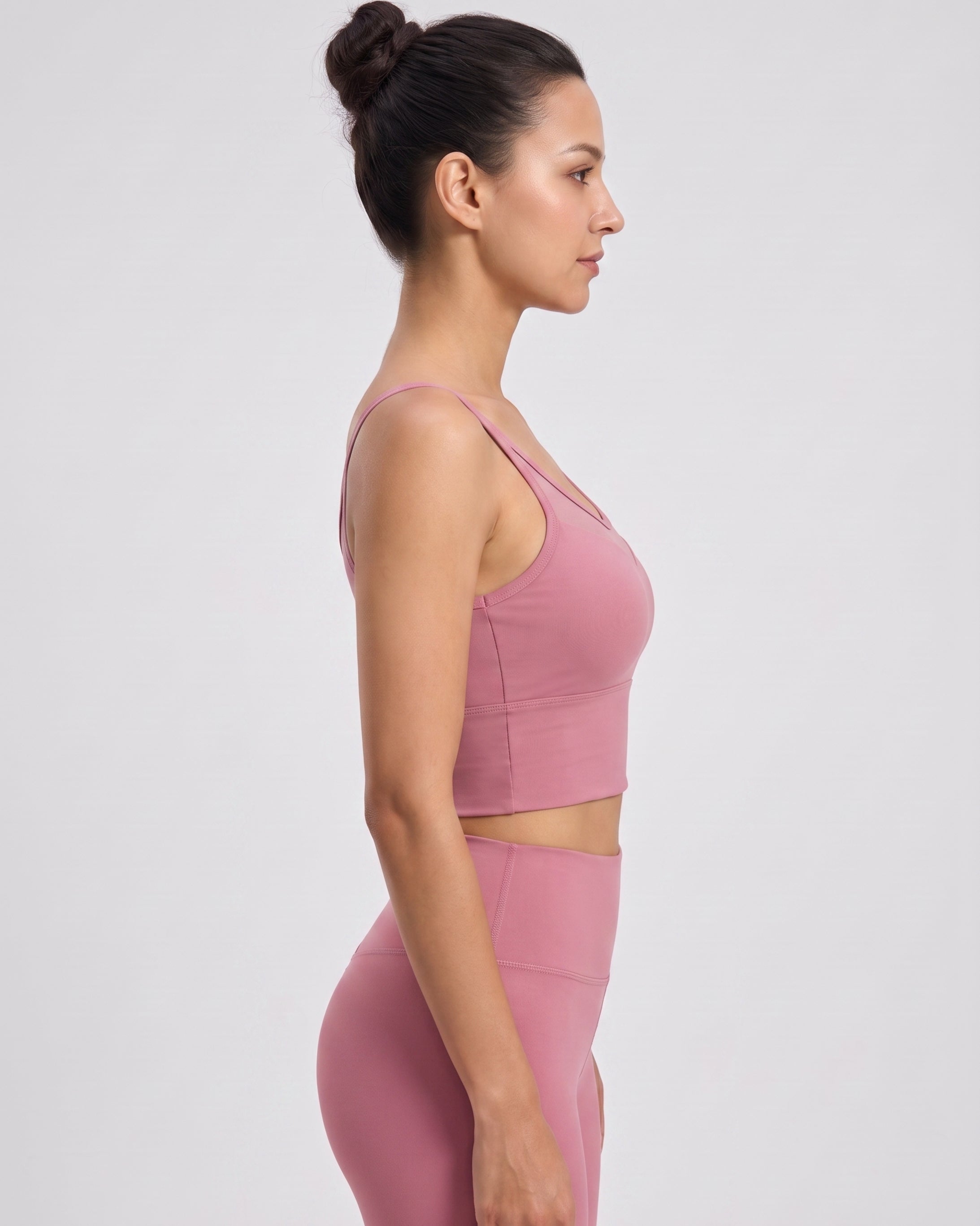 A woman in side profile wearing a matching dusty pink activewear set, featuring a sports bra and high-waisted leggings, against a plain light gray studio background.