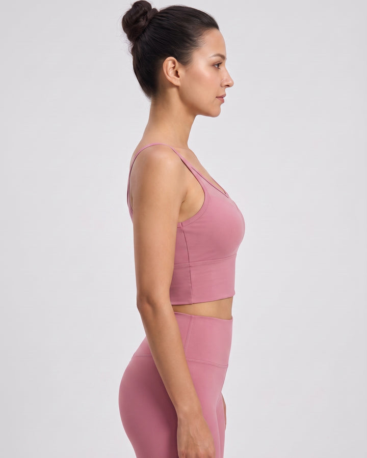 A woman in side profile wearing a matching dusty pink activewear set, featuring a sports bra and high-waisted leggings, against a plain light gray studio background.