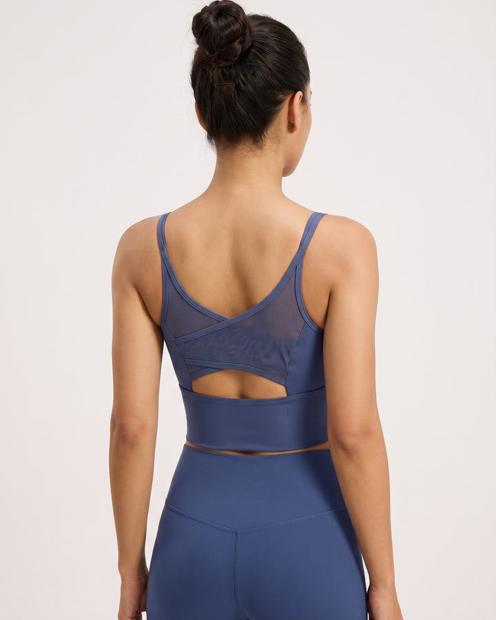 A woman shown from the back wearing a slate blue activewear set, featuring a sports bra with a mesh criss-cross back design and a cutout, paired with matching high-waisted leggings.