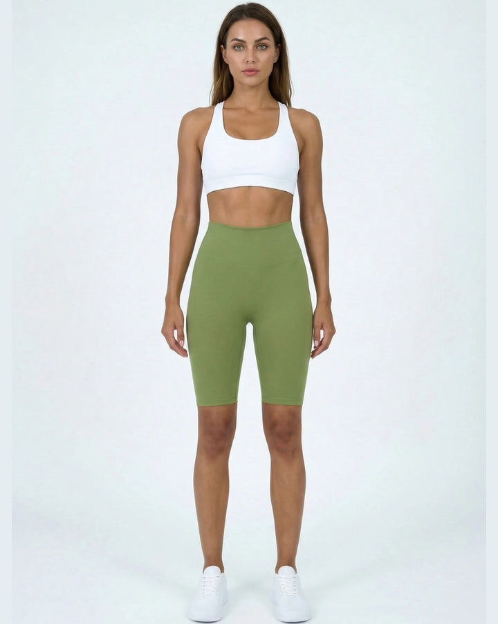 Woman wearing a white sports bra and green high-waisted shorts on a white background