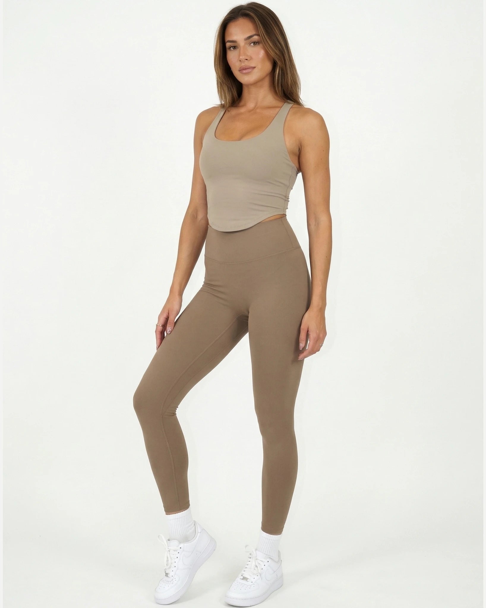 Woman wearing a beige tank top and leggings set on a white background