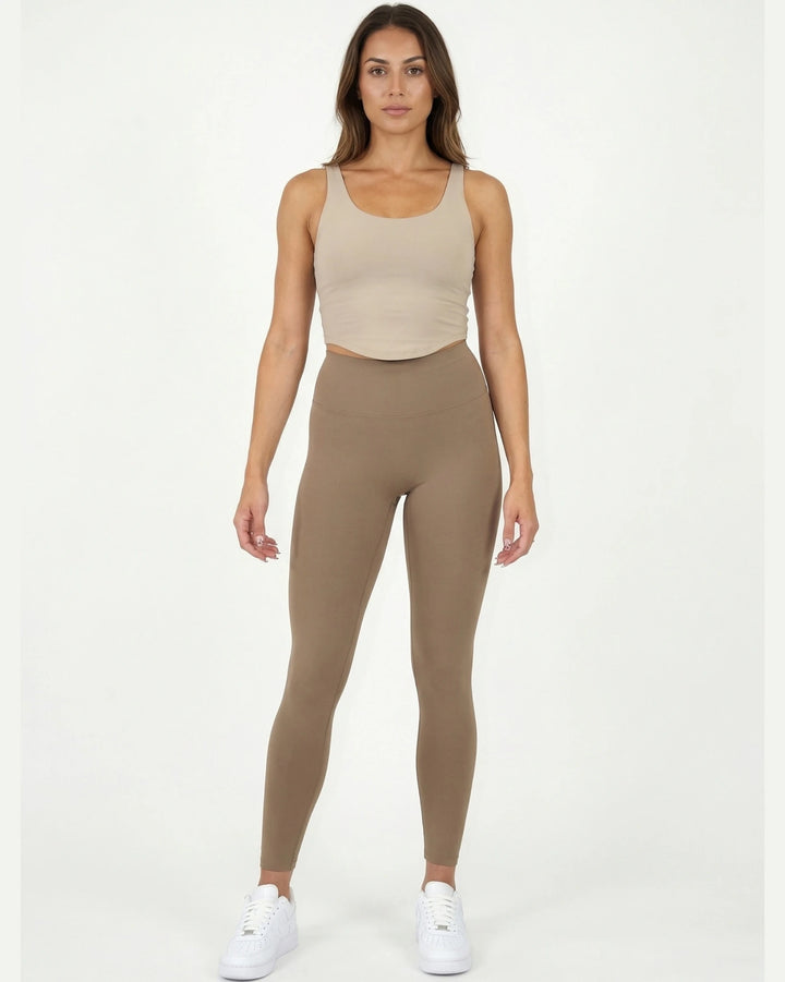 Woman wearing a beige tank top and leggings on a white background