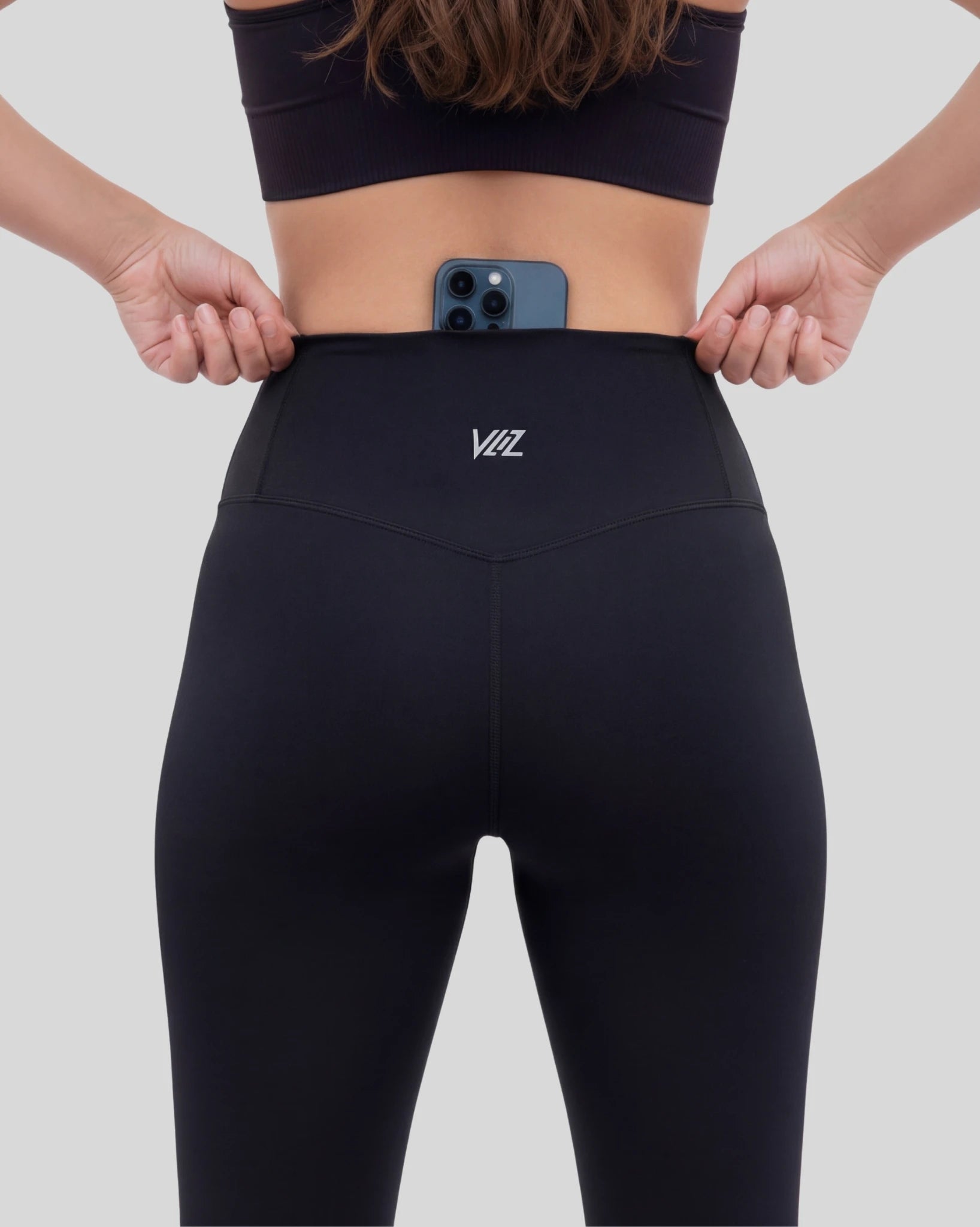 Person wearing black leggings with a logo, holding a phone with a white background