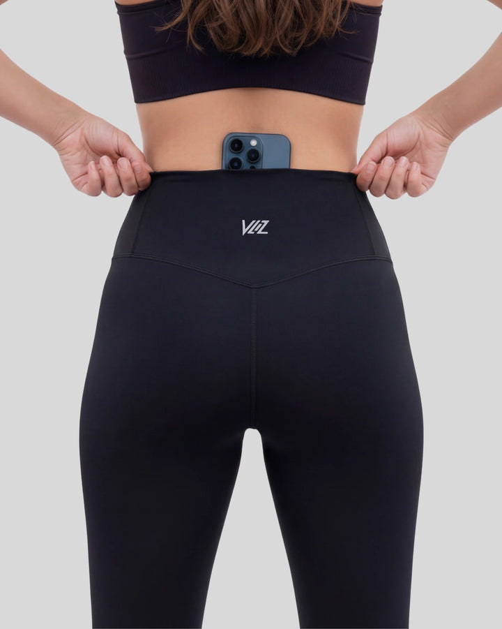 Person wearing black leggings with a logo, holding a phone with a white background