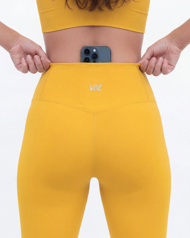 Person wearing yellow leggings with a brand logo, holding a phone, on a white background
