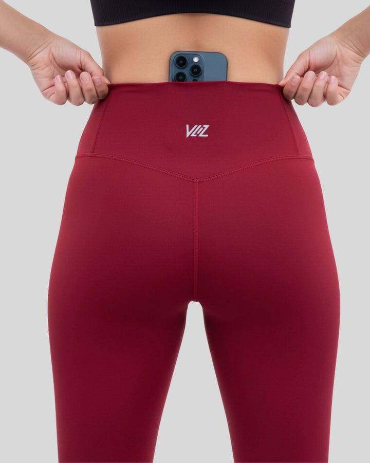 Red leggings with a brand logo being held up by hands on a light gray background
