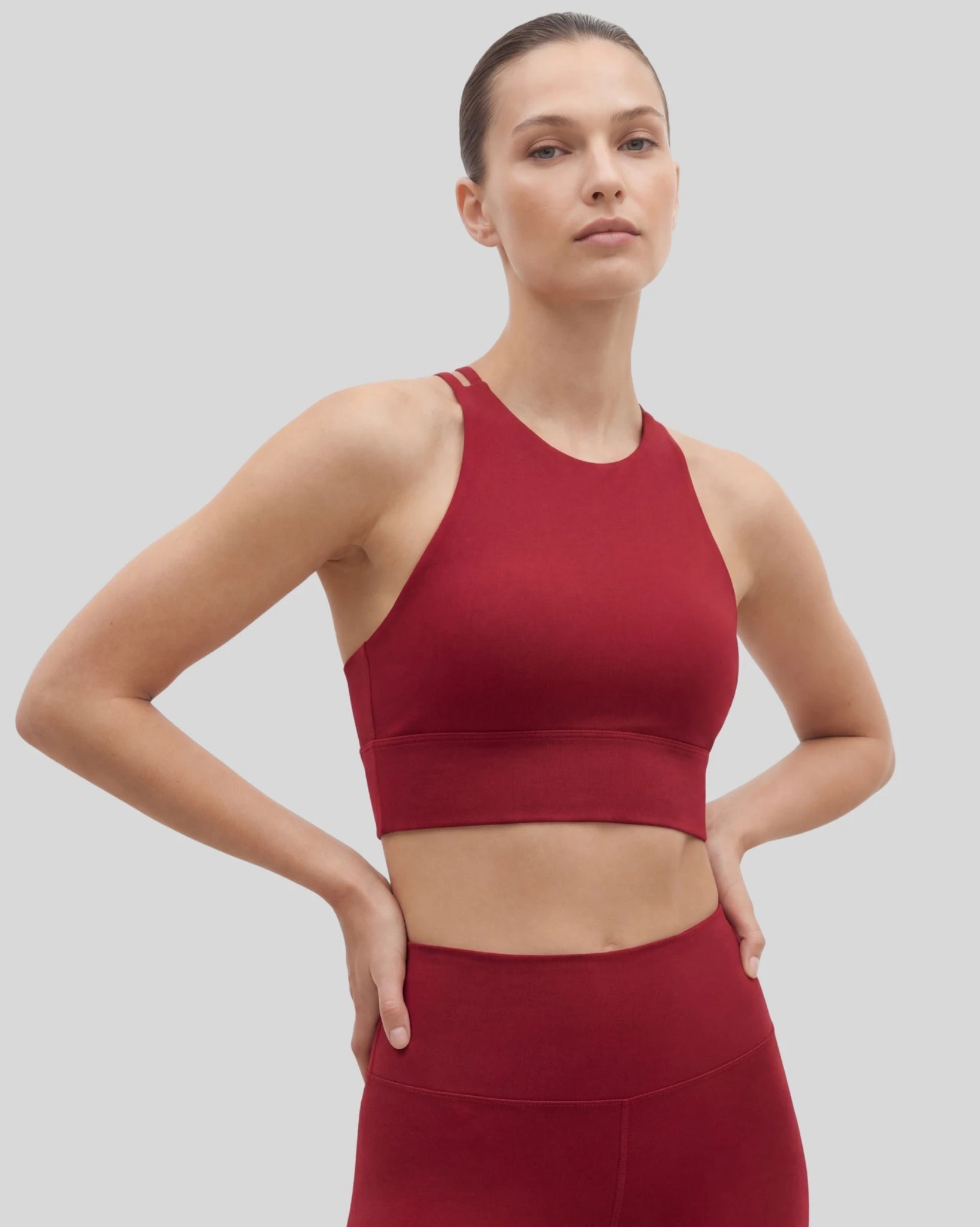 Woman wearing a red sports bra and leggings on a light gray background
