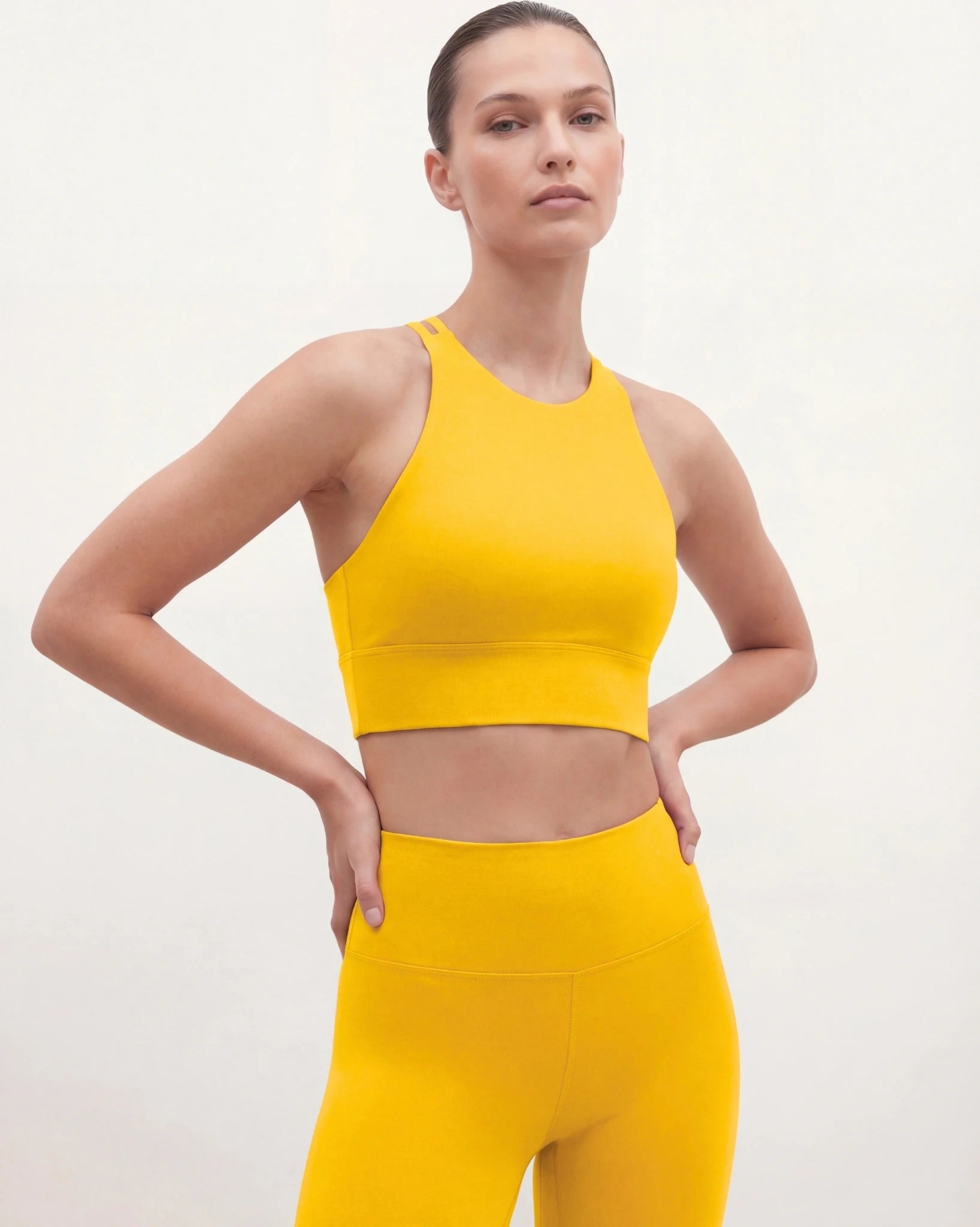 Woman wearing a yellow sports bra and leggings on a white background