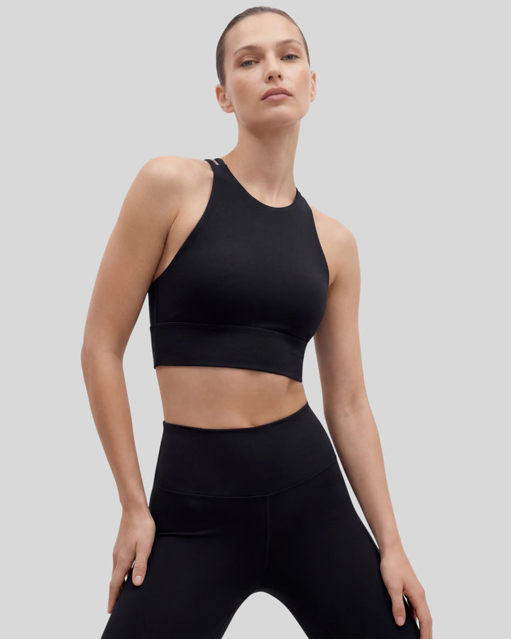 Woman wearing a black sports bra and leggings on a light gray background