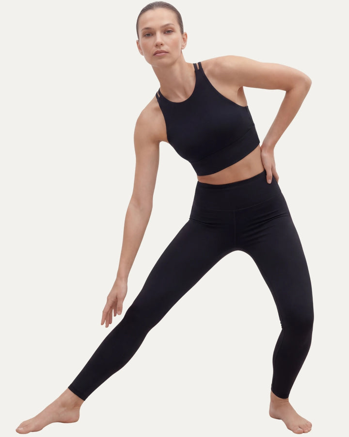 Woman wearing black athletic leggings and sports bra on a light gray background