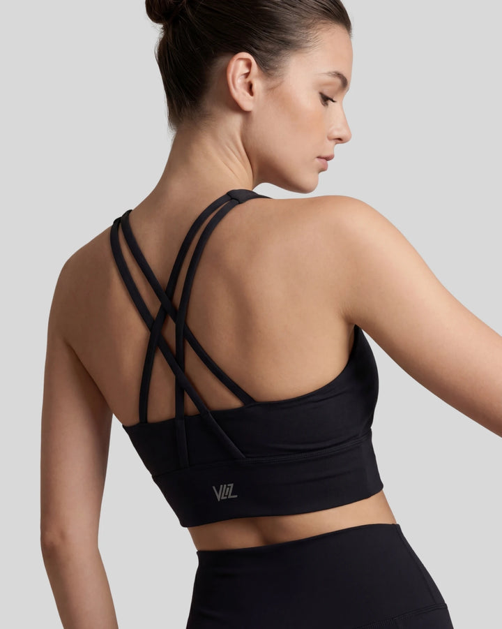 Woman wearing a black sports bra with criss-cross straps on a light gray background