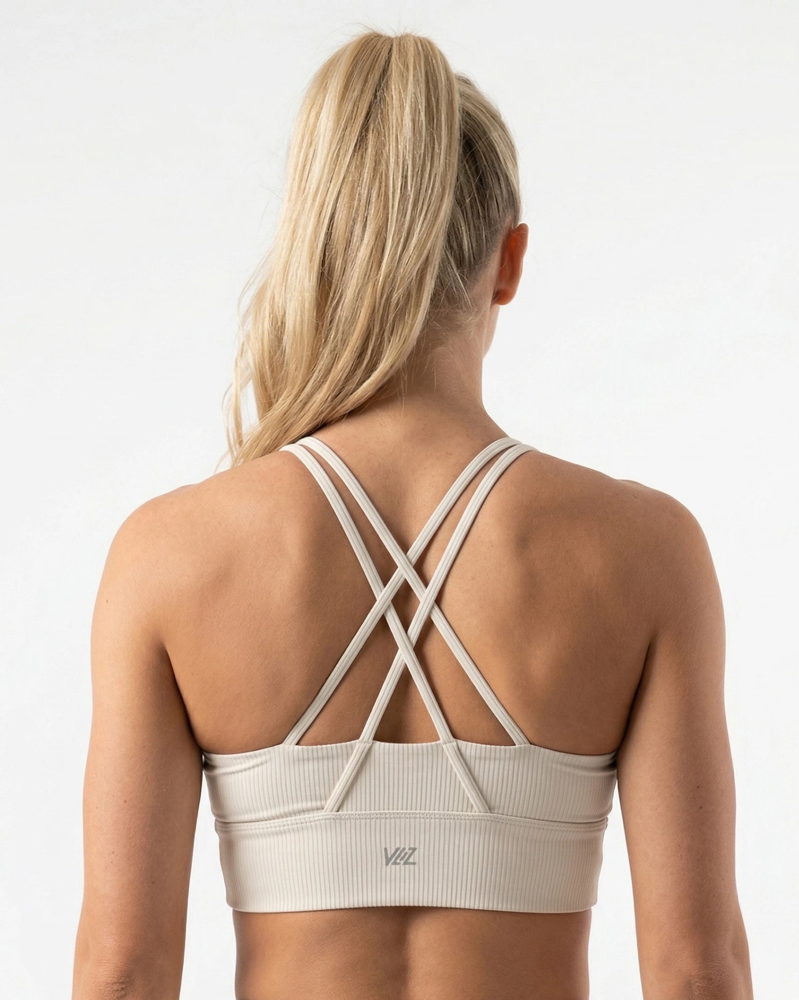 Beige sports bra with criss-cross straps worn by a person on a white background