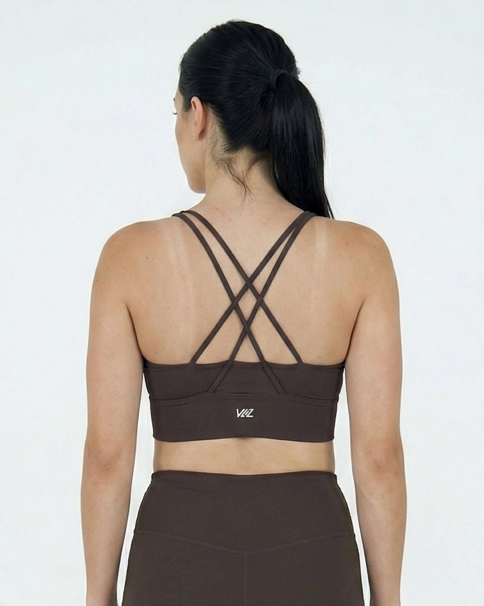 Woman wearing a brown sports bra with criss-cross straps on a white background
