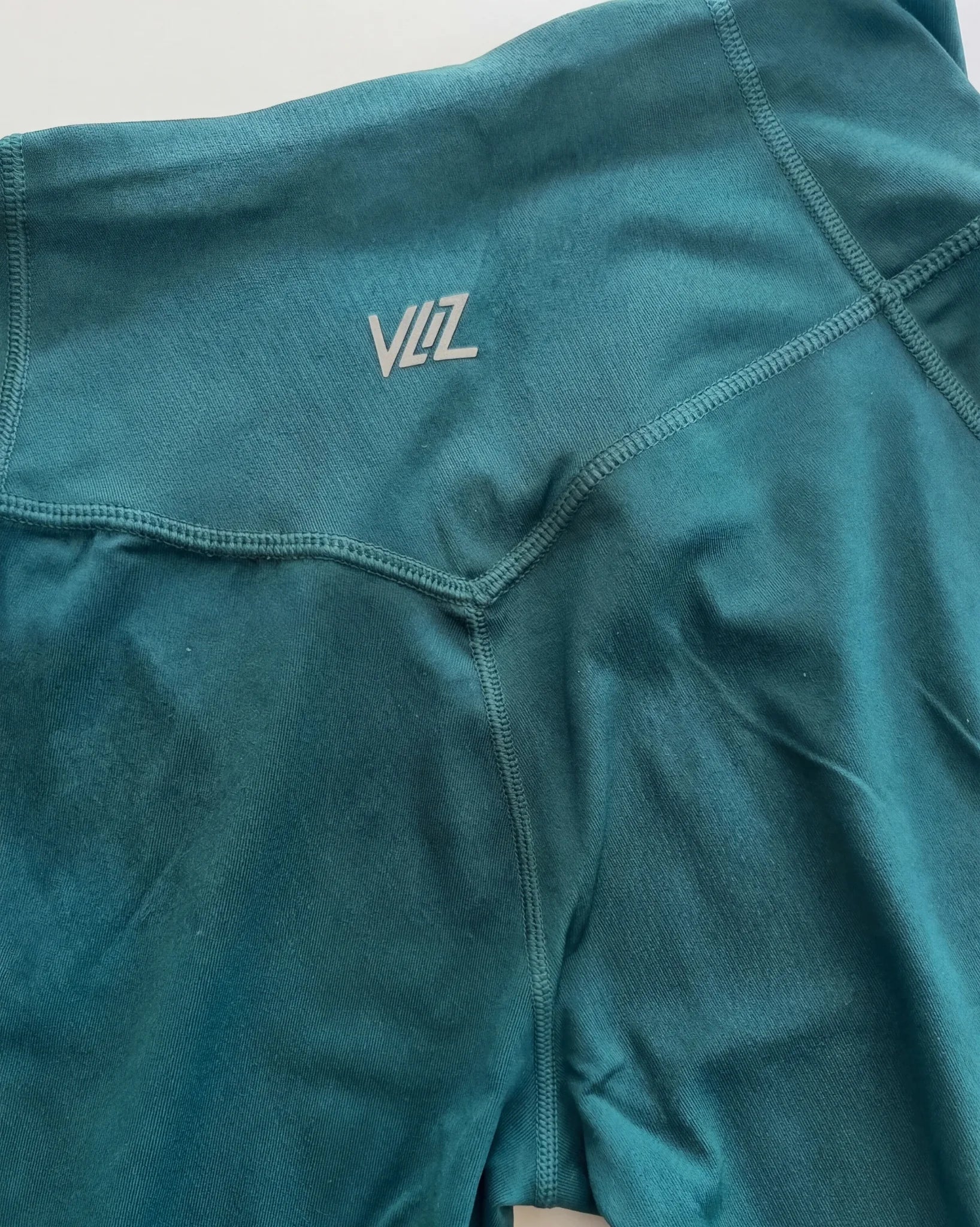 Teal athletic shirt with a logo on the chest against a light gray background
