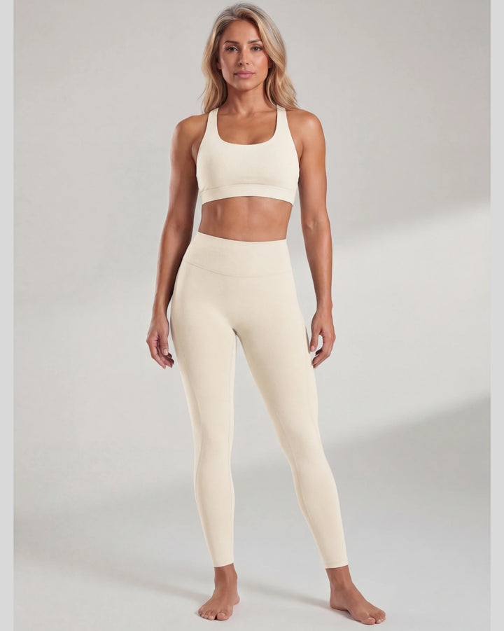 Woman wearing a beige sports bra and leggings set on a plain background