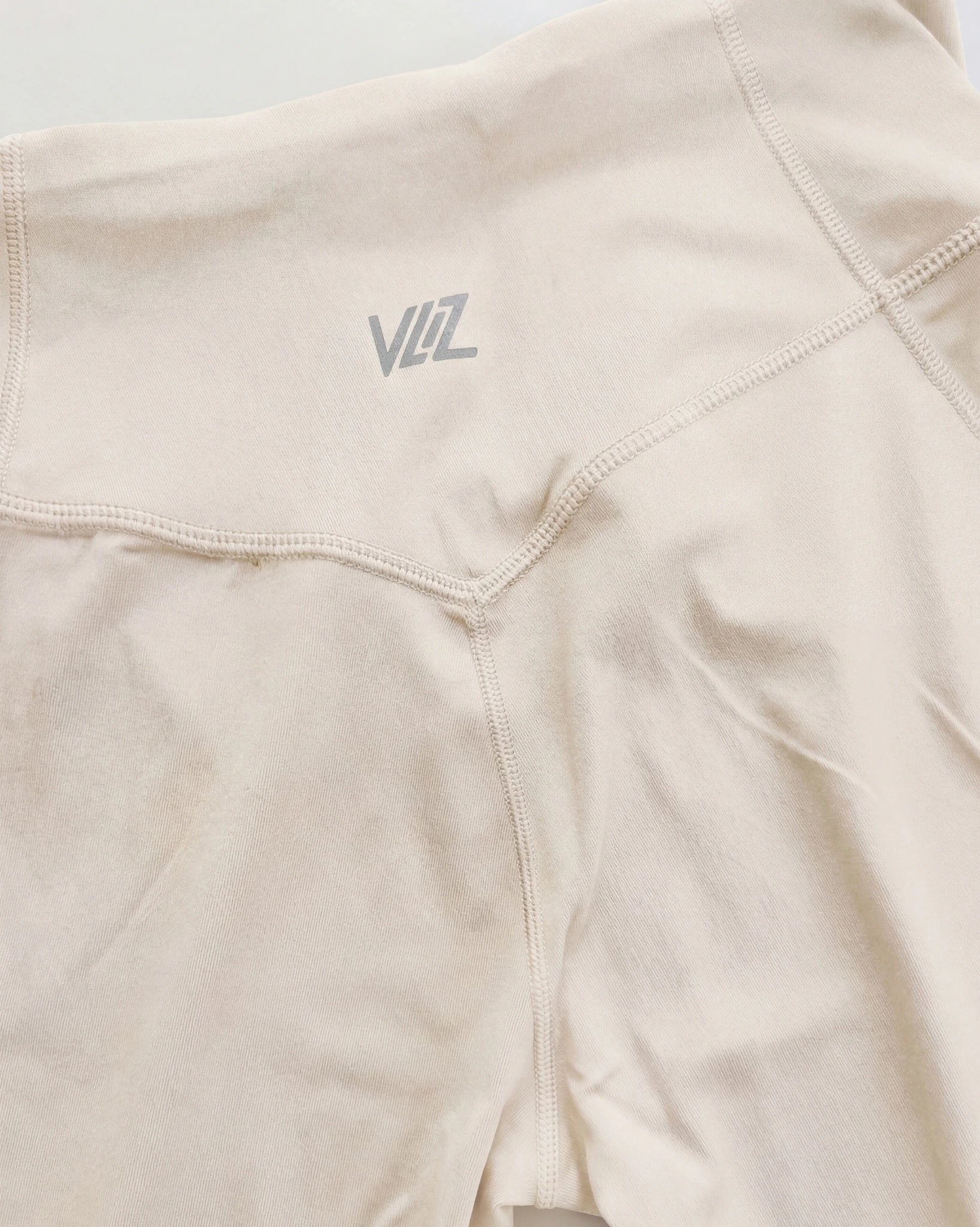 Beige athletic shorts with a brand logo on a light gray background