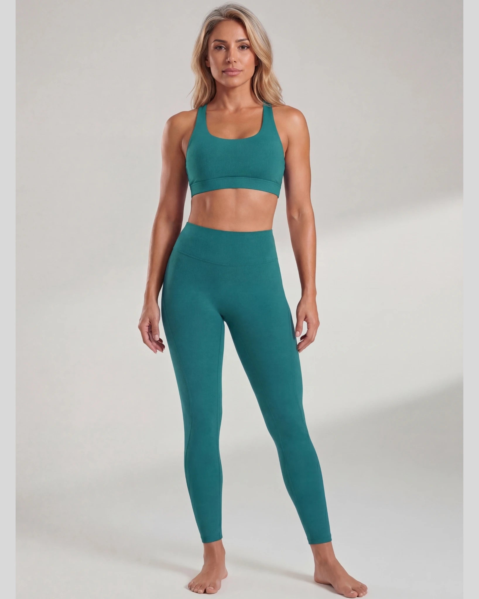 Woman wearing teal sports bra and leggings on a plain background