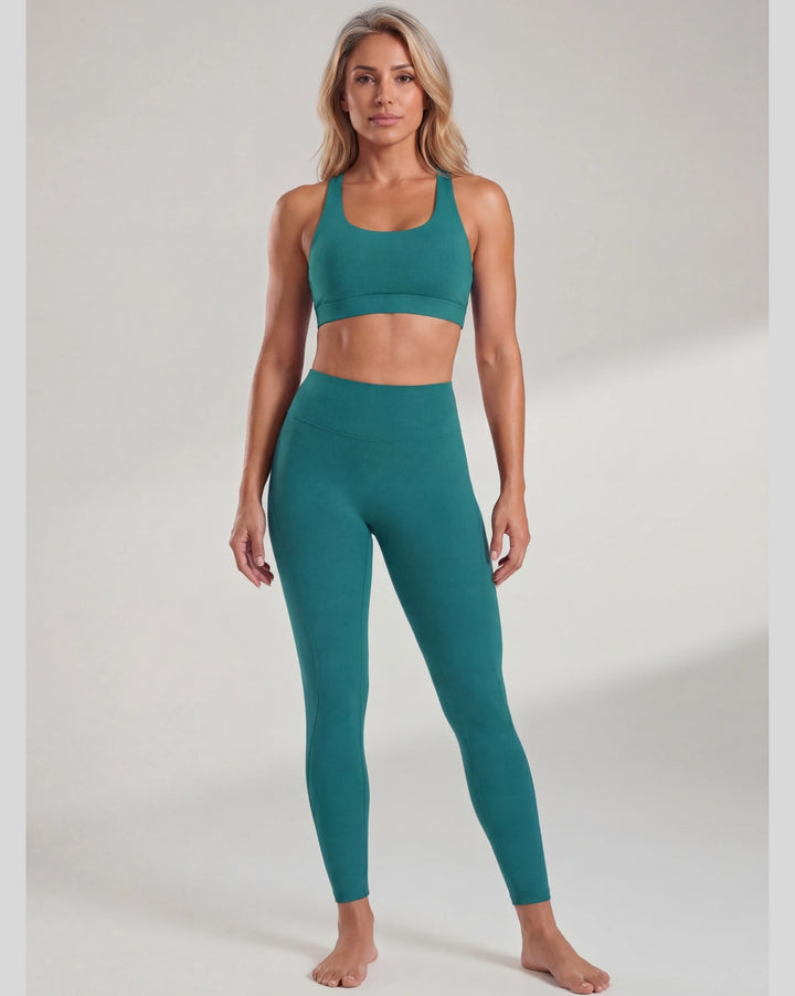 Woman wearing teal sports bra and leggings on a plain background