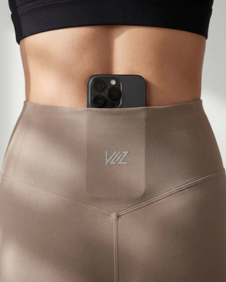 Person wearing beige leggings with a pocket featuring a logo, holding a phone.