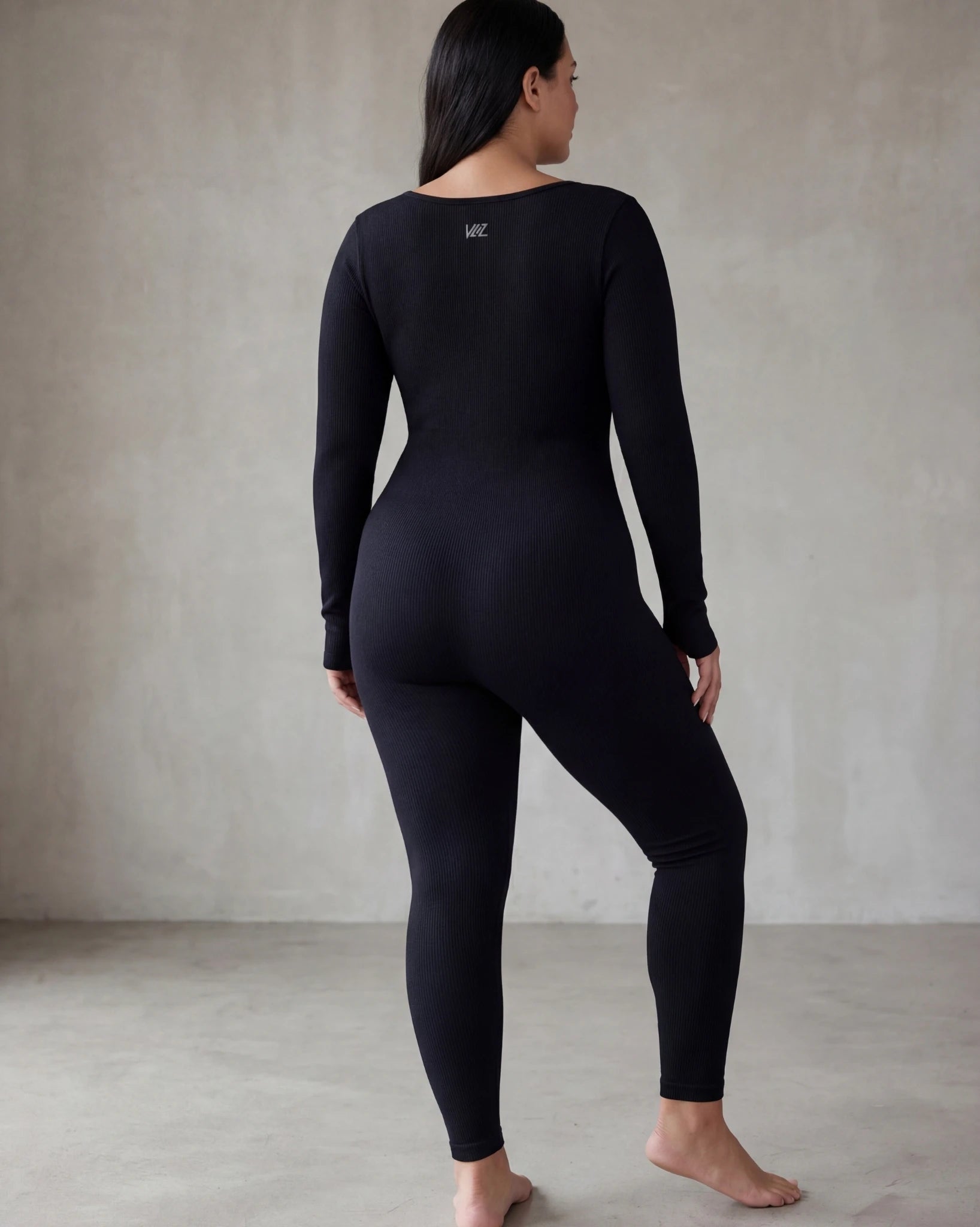 Person wearing a black bodysuit against a plain background