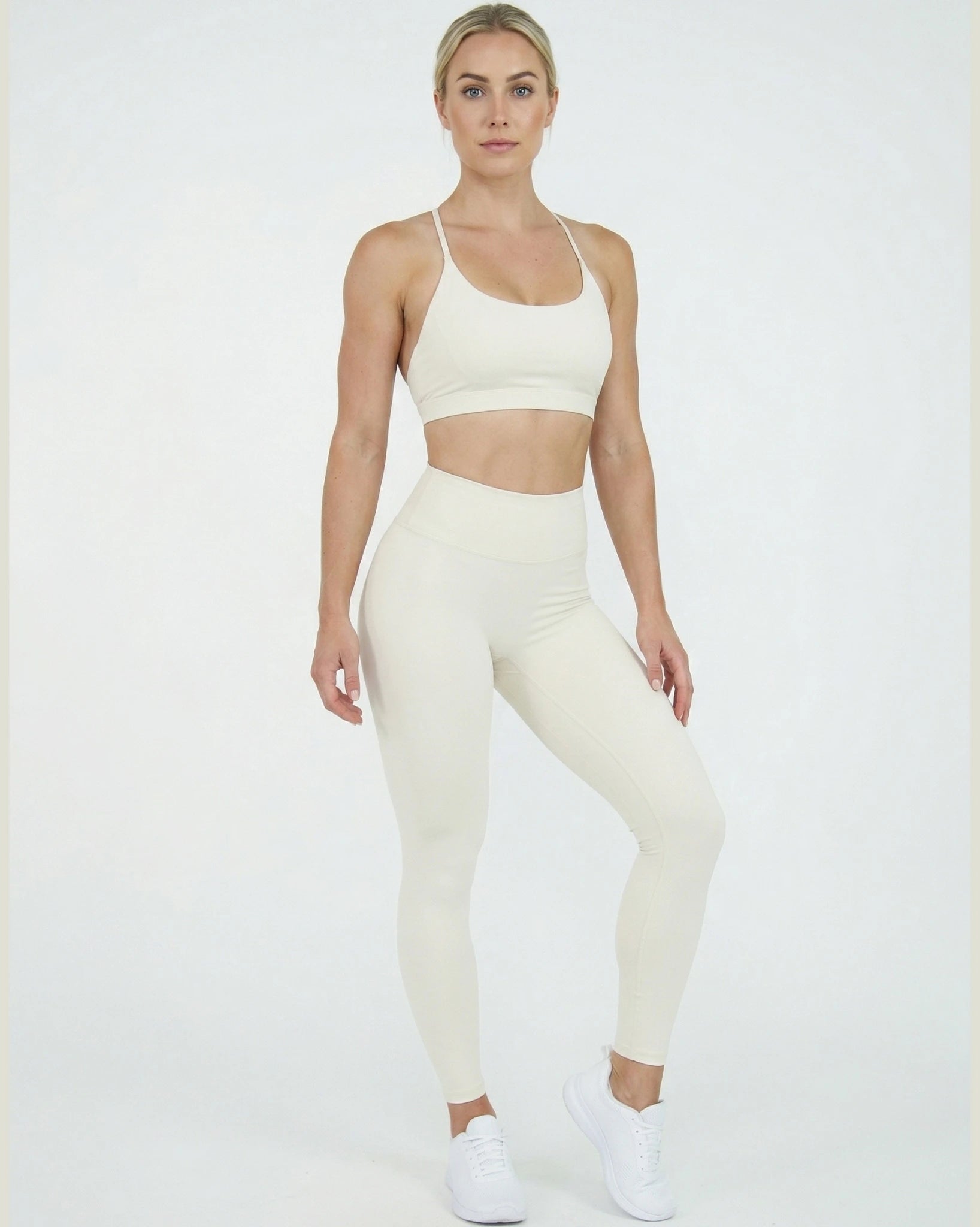 Woman wearing a white sports bra and leggings set on a white background